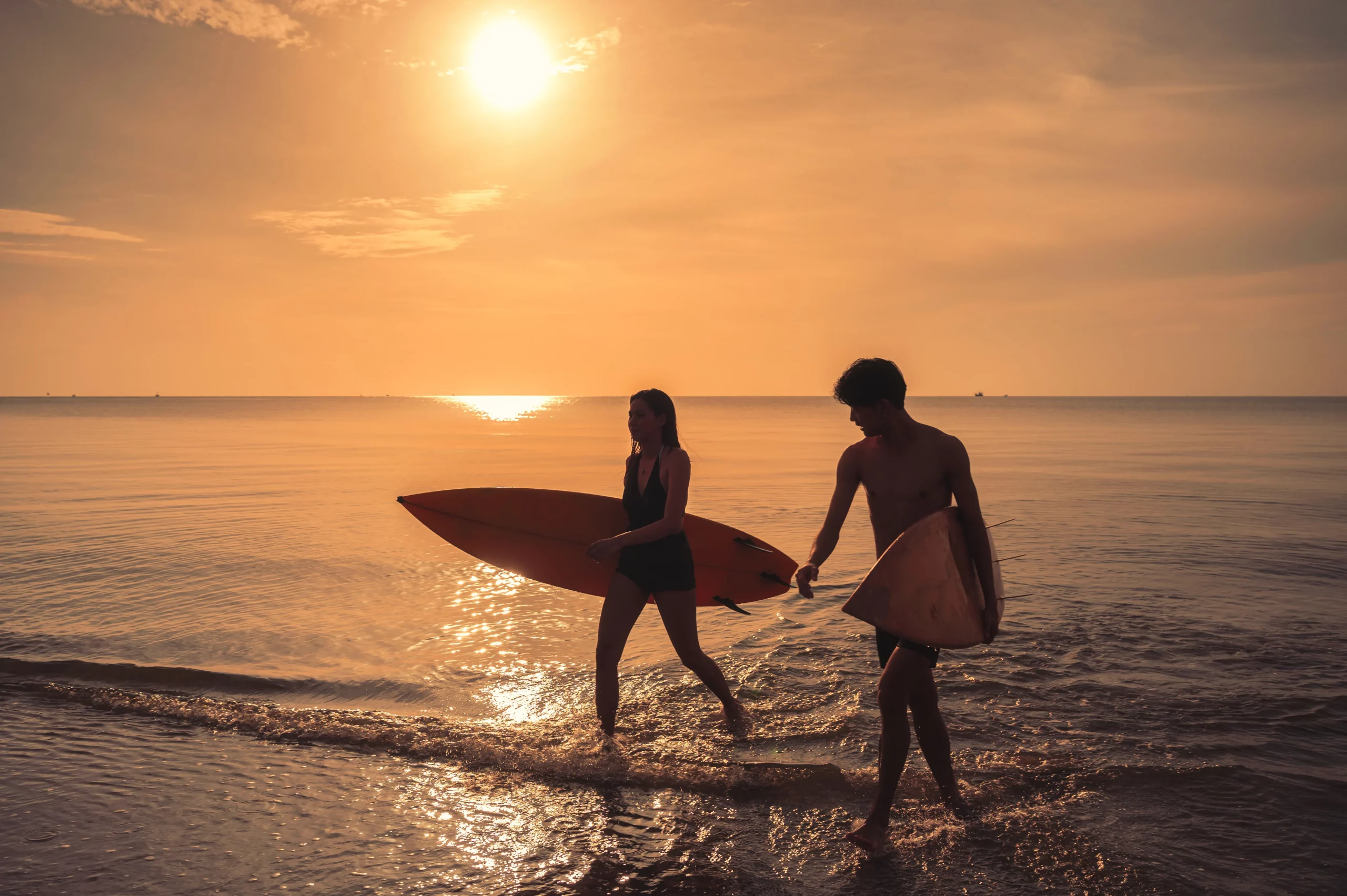 Couple walking out of the ocean with surfboards at sunset on a beach near Lisbon, highlighting coastal activities and nature experiences beyond the city