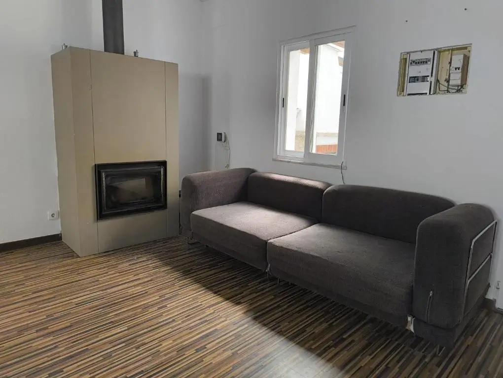 Modern living room with a comfortable gray sofa, fireplace, and natural lighting at AkiStay guesthouse in Costa da Caparica near Lisbon, providing a warm and relaxing atmosphere for guests.