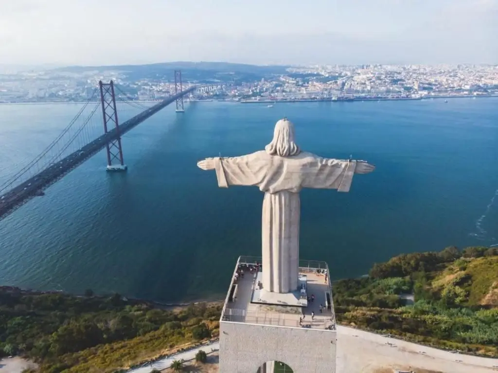 Aerial view of Cristo Rei statue overlooking the 25 de Abril Bridge and Lisbon cityscape.