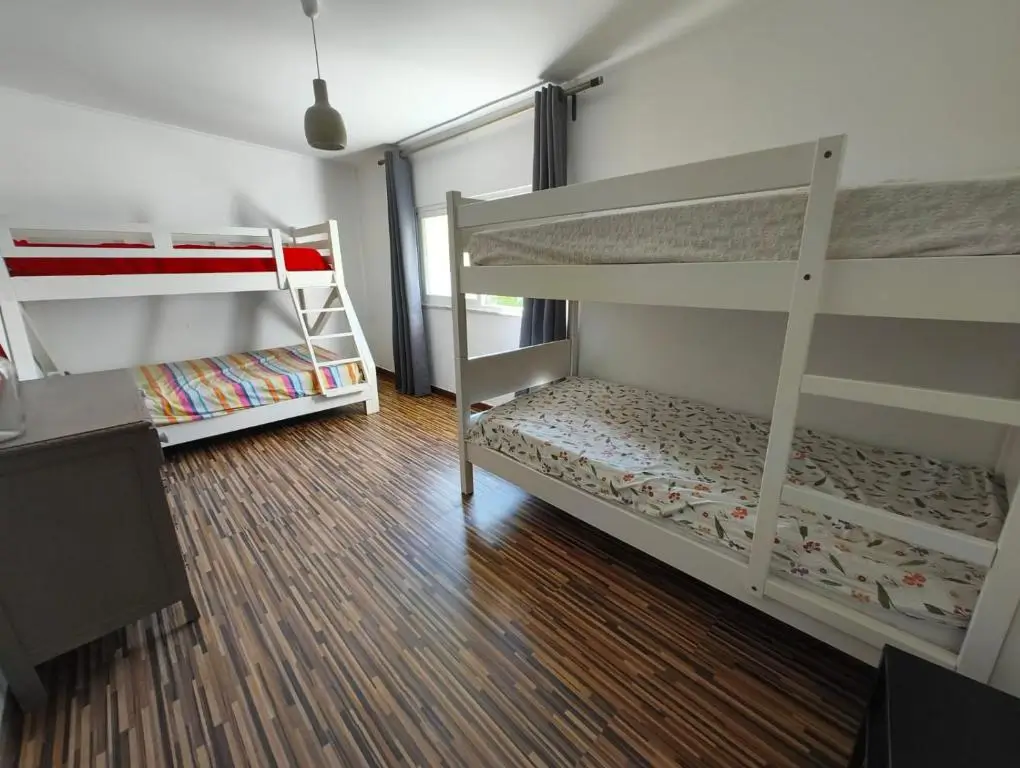 Bright family room with modern white bunk beds, large window, and wooden flooring at AkiStay guesthouse in Costa da Caparica near Lisbon, ideal for families and group stays close to the beach.