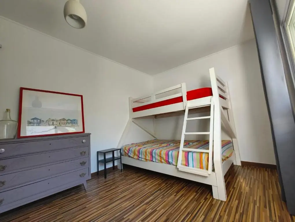 Bright family room featuring a modern white bunk bed with colorful striped bedding, wooden flooring, and decorative touches at AkiStay guesthouse in Costa da Caparica near Lisbon, offering a cheerful and comfortable stay for families.