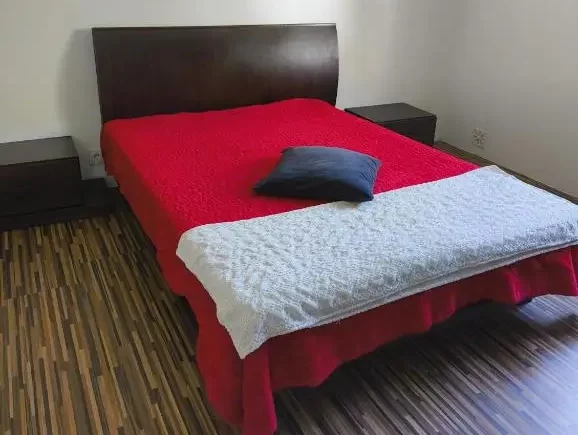 Cozy double bedroom with red bedding, dark wooden headboard, and matching bedside tables at AkiStay guesthouse in Costa da Caparica near Lisbon, offering modern comfort and stylish accommodation for couples or solo travelers.