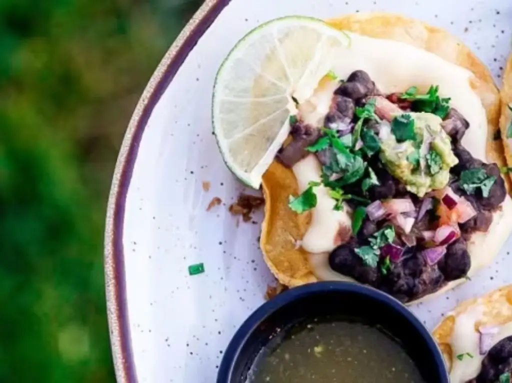 Close-up of Portuguese-style tapas with beans, guacamole, and lime served on a white plate outdoors.